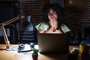 Poster - Young brunette woman with curly hair working at the office at night laughing and embarrassed giggle covering mouth with hands, gossip and scandal concept