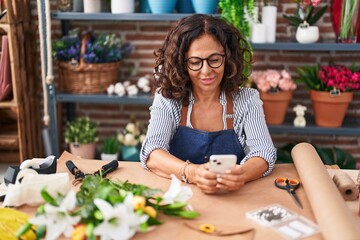 Wall Mural - Middle age woman florist smiling confident using smartphone at flower shop