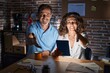 © Krakenimages.com - Middle age hispanic couple using touchpad sitting on the table at night smiling friendly offering handshake as greeting and welcoming. successful business.
