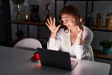 Wall Mural - Middle age hispanic woman using laptop at home at night showing and pointing up with fingers number seven while smiling confident and happy.