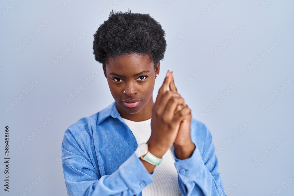 African american woman standing over blue background holding symbolic gun with hand gesture, playing killing shooting weapons, angry face