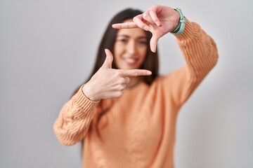 Sticker - Young brunette woman standing over white background smiling making frame with hands and fingers with happy face. creativity and photography concept.