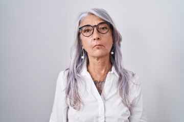 Wall Mural - Middle age woman with tattoos wearing glasses standing over white background relaxed with serious expression on face. simple and natural looking at the camera.