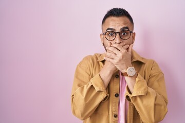 Poster - Young hispanic man standing over pink background shocked covering mouth with hands for mistake. secret concept.