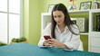 © Krakenimages.com - Young beautiful hispanic woman using smartphone sitting on table at dinning room