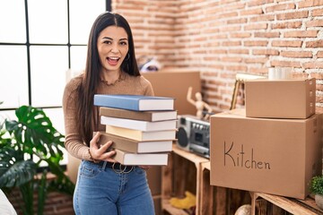 Canvas Print - Young woman holding books at home celebrating crazy and amazed for success with open eyes screaming excited.