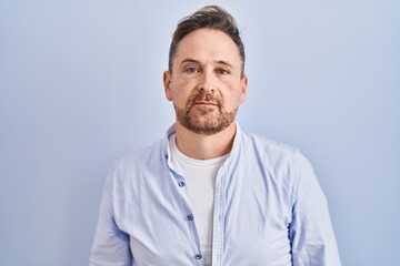 Poster - Middle age caucasian man standing over blue background relaxed with serious expression on face. simple and natural looking at the camera.