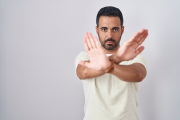 Wall Mural - Hispanic man with beard standing over isolated background rejection expression crossing arms and palms doing negative sign, angry face