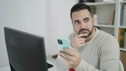 Sticker - Young hispanic man student using computer and smartphone at library university