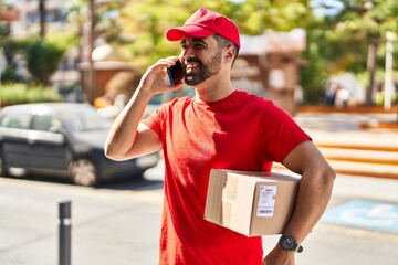 Sticker - Young hispanic man courier talking on the smartphone holding package at street