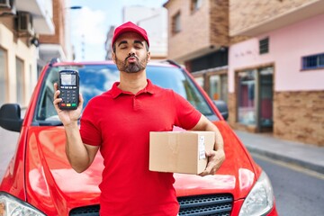 Sticker - Young hispanic man with beard wearing delivery uniform and cap holding dataphone looking at the camera blowing a kiss being lovely and sexy. love expression.