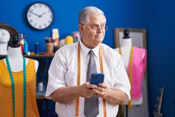 Canvas Print - Middle age grey-haired man tailor smiling confident using smartphone at tailor shop