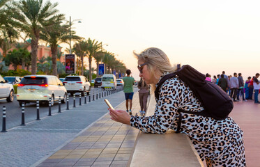 Wall Mural - The photo shows a beautiful blonde tourist who enjoys the hospitality of Dubai. Her smile is bright and welcoming, and her hair is flying in the wind, giving her a certain playfulness.