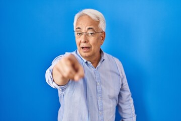 Poster - Hispanic senior man wearing glasses pointing with finger surprised ahead, open mouth amazed expression, something on the front