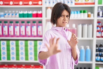 Wall Mural - Young girl at pharmacy drugstore disgusted expression, displeased and fearful doing disgust face because aversion reaction. with hands raised