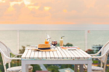 Luxury breakfast table for two with tropical sea view background. Perfect setting for romantic vacation or honeymoon. Elegant decoration, glasses, straw hat, and delicious food in paradise.