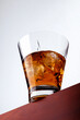 Wonderfull closeup macro photo of a shiny glass with stunning alcohol whiskey shot and a few cubes of ice on a brown wooden board with white background shot in the studio