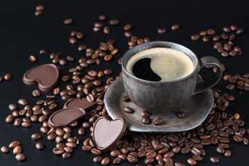 Wall Mural - Grey brown grunge cup of fresh hot coffee with beans and dark chocolate pieces on black background.