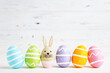 Egg with rabbit face and row colorful easter eggs on white wooden background
