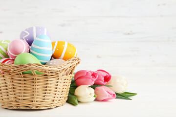 Wall Mural - Colorful easter eggs in basket and bouquet of tulips on white wooden background