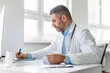 © Prostock-studio - Middle aged male doctor sitting at table in office hospital, therapist man practitioner writing and working in clinic