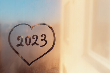 Wall Mural - numbers 2023 of new year in heart shape paint with finger on splashed by rain foggy sunset glass on window