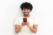 © kucherav - Smiling Asian student man in a white t-shirt hold in hands use mobile cell phone, sends a message, chatting online standing isolated on white background