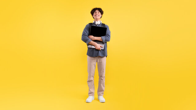 Wall Mural - Happy Male Student Hugging New Laptop Standing Over Yellow Background