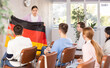 © JackF - Female teacher tells the history of the state of Germany, holding the national flag of Germany in his hands