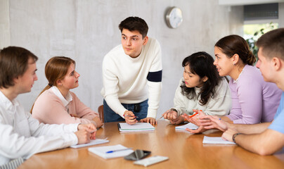 Positive motivated young guy, student team leader holding meeting with group, explaining details of new study project