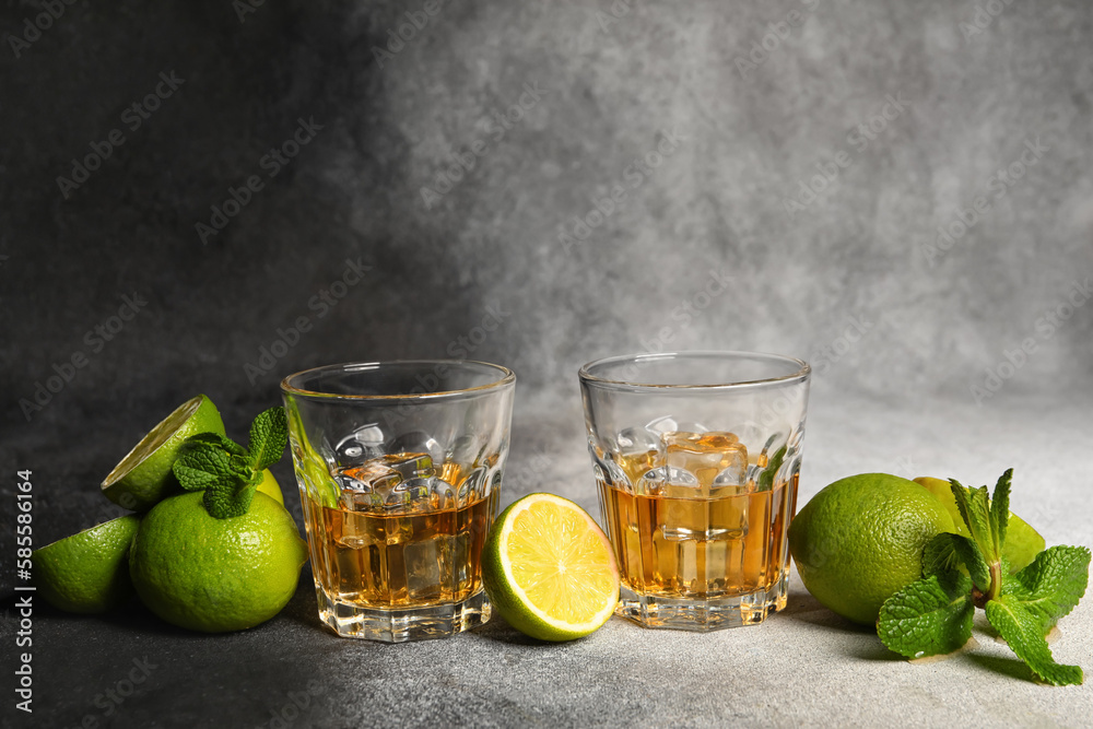 Glasses of rum with ice, mint and lime on grey background