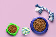 Bowls with dry pet food and toys on color background