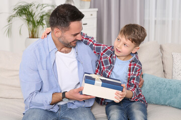 Poster - Cute little boy presenting his father with gift on sofa at home