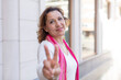 © kues1 - middle age woman smiling and looking happy, carefree and positive, gesturing victory or peace with one hand