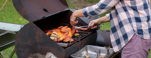 Senior woman grilling chicken meat for preparing eat in camping, elderly doing activity recreation and leisure picnic while roasting meat in weekend, travel trip in holiday, party in vacations.