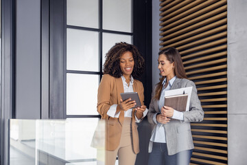 Two female collegues standing next to each other in modern office