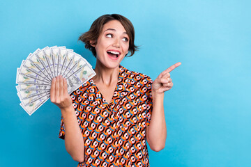 Photo of shocked funny lady dressed print shirt rising cash fan looking pointing empty space isolated blue color background