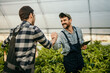 Two farmers standing in a field in the greenhouse. Two men talking and handshaking while using tablet technology for agriculture.