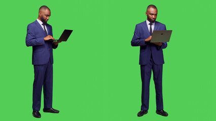 Modern employee using laptop to browse network, looking at online website standing over full body greenscreen. Young adult businessman working with wireless computer in studio.