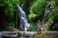 Hiker Girl Stands Gazing At An Amazing Tropical Waterfall (elabana Falls) In Lamington National Park Near Gold Coast And Brisbane In Queensland, Australia; Rainforest Waterfall Amidst Lush Vegetation