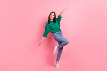 Full length photo of pleasant adorable girlish person wear jeans green shirt flying having fun arms like wings isolated on pink background