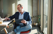 © Westend61 - Happy businessman using laptop and holding tablet PC in office
