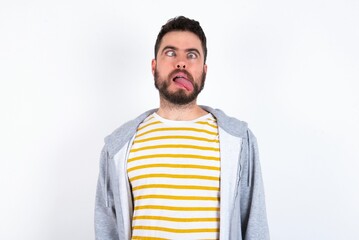 Young caucasian mán wearing trendy clothes over white background showing grimace face crossing eyes and showing tongue. Being funny and crazy