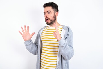 Wall Mural - Young caucasian mán wearing trendy clothes over white background shouts loud, keeps eyes opened and hands tense.