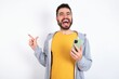 © Jihan - Astonished Young caucasian mán wearing trendy clothes over white background holding her telephone and pointing with finger aside at empty copy space