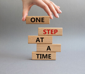 Wall Mural - One step at a time symbol. Concept words One step at a time on wooden blocks. Beautiful grey background. Businessman hand. Business and One step at a time concept. Copy space.