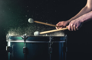 Wall Mural - A man plays a musical percussion instrument with sticks on a dark background.