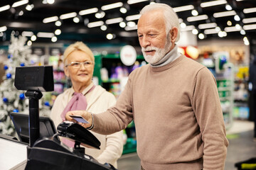 Wall Mural - An old man in paying on self-service cash register at the supermarket.