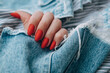 Beautiful female hands with a bright red matte manicure on a background of denim. Stylish oval nail design. Summer manicure. Copy space.