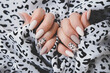 A woman's hand with a beautiful manicure holds a fabric with a leopard print. Autumn trend, beige color polishing with leopard pattern on nails with gel polish, shellac.